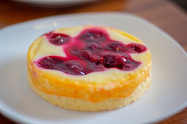 Tahta masadaki beyaz tabakta kirazlı cheesecake..