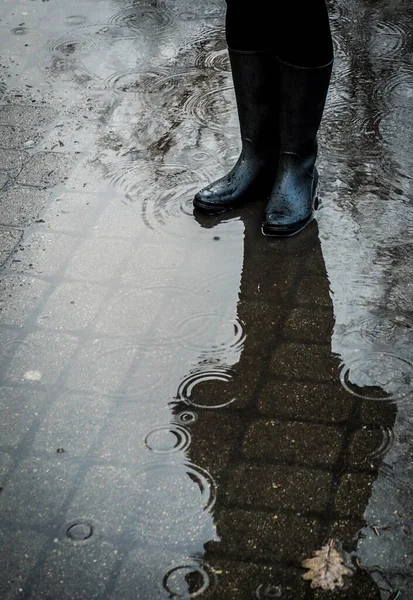 Chica de pie en charco en botas de goma negro durante la lluvia — Foto de Stock