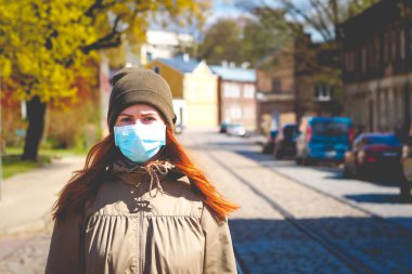 Sokakta yüzü maske takmış, kızıl saçlı, güzel Avrupalı bir kadın. Coronavirus enfeksiyonuna karşı korunmak için solunum cihazına bağlı genç bir dişinin görüntüsü.