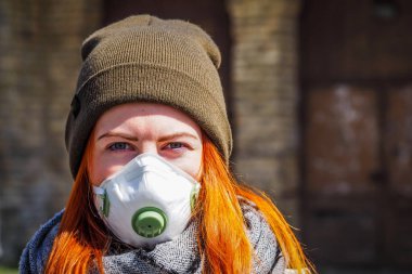 Sokakta yüzü maske takmış, kızıl saçlı, güzel Avrupalı bir kadın. Coronavirus enfeksiyonuna karşı korunmak için solunum cihazına bağlı genç bir dişinin görüntüsü.
