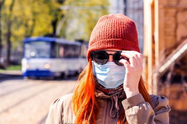 Sokakta yüzü maske takmış, kızıl saçlı, güzel Avrupalı bir kadın. Coronavirus enfeksiyonuna karşı korunmak için solunum cihazına bağlı genç bir dişinin görüntüsü.