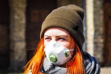 Sokakta yüzü maske takmış, kızıl saçlı, güzel Avrupalı bir kadın. Coronavirus enfeksiyonuna karşı korunmak için solunum cihazına bağlı genç bir dişinin görüntüsü.
