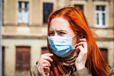 Sokakta yüzü maske takmış, kızıl saçlı, güzel Avrupalı bir kadın. Coronavirus enfeksiyonuna karşı korunmak için solunum cihazına bağlı genç bir dişinin görüntüsü.