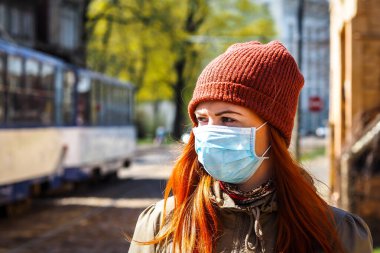 Sokakta yüzü maske takmış, kızıl saçlı, güzel Avrupalı bir kadın. Coronavirus enfeksiyonuna karşı korunmak için solunum cihazına bağlı genç bir dişinin görüntüsü.