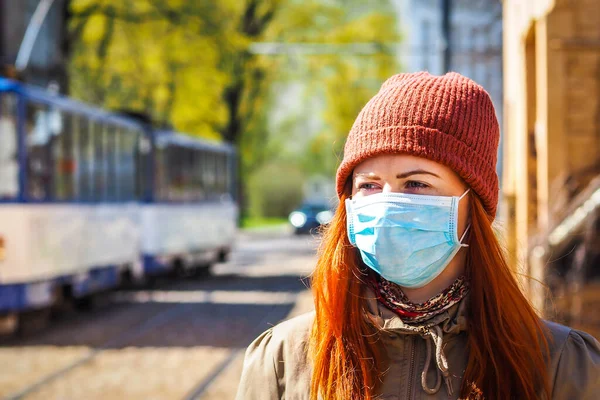 Sokakta yüzü maske takmış, kızıl saçlı, güzel Avrupalı bir kadın. Coronavirus enfeksiyonuna karşı korunmak için solunum cihazına bağlı genç bir dişinin görüntüsü.
