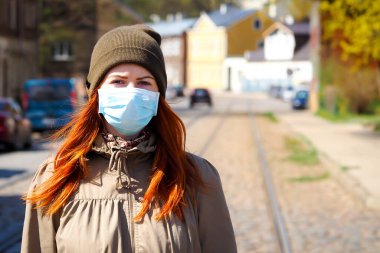 Sokakta kızıl saçlı, yüzü tıbbi maske takmış güzel Avrupalı bir kadın.