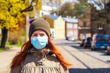 Sokakta kızıl saçlı, yüzü tıbbi maske takmış güzel Avrupalı bir kadın.