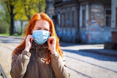 Sokakta kızıl saçlı, yüzü tıbbi maske takmış güzel Avrupalı bir kadın.
