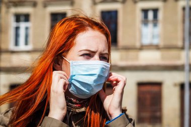Sokakta kızıl saçlı, yüzü tıbbi maske takmış güzel Avrupalı bir kadın.