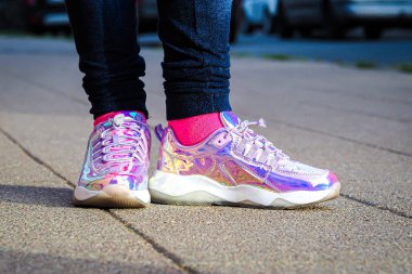 Kız bacaklarında mor holografik spor ayakkabılar, arka planda şehir, seçici odak
