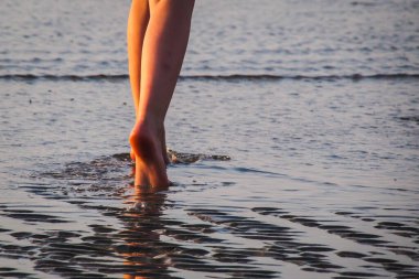 Yaz akşamında kız gün batımında kız denizde yürüyor, kız bacakları, seçici odaklanma.