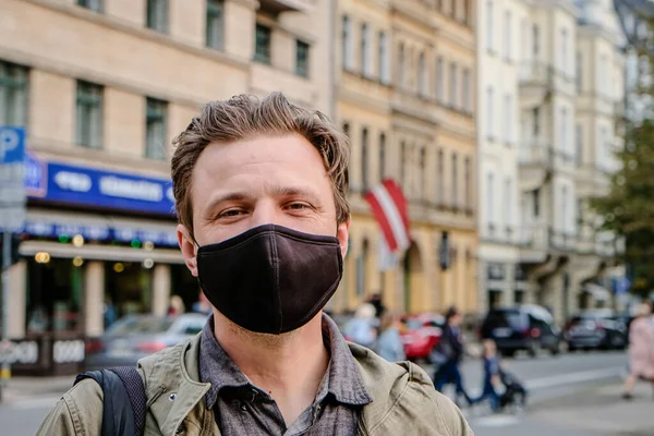 Bonito jovem europeu numa rua com uma máscara preta. Closeup de um homem de 35 anos em um respirador para proteger contra coronavírus — Fotografia de Stock