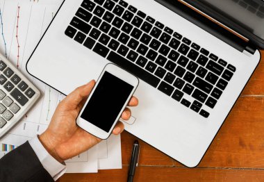 El Smartphone dizüstü bilgisayar ve ofis araçları ile ahşap arka plan üzerinde gündoğumu içinde tutarak.