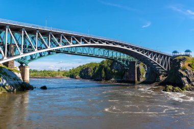Saint John, New Brunswick, Kanada 'daki Reversing Falls köprüsü, Saint John nehri üzerinde. Nehir yavaşça dışarıya akıyor. Tren köprüsü arkada, mavi gökyüzü yukarıda. Düşük açı görünümü.