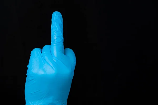 A blue gloved hand with middle finger extended. The glove is blue latex. Black background.