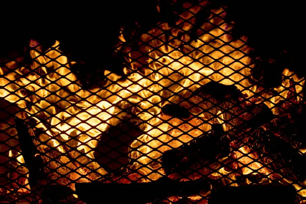 An outdoor fire in a heavy screen fireplace at night. Scene is dark except for the flames. Focus is on the burning wood embers.