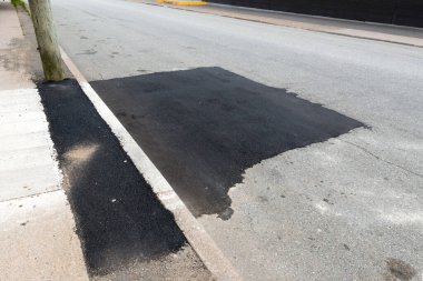Koyu siyah asfalt ile kaplanmış gri soluk bir sokak. Kaldırımın bir kısmı da yamalı..
