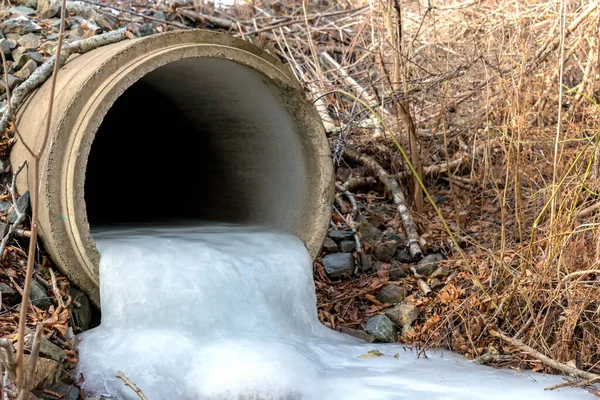 Looking into a frozen culvert. The pipe is about a quarter full of ice which flows out the end.
