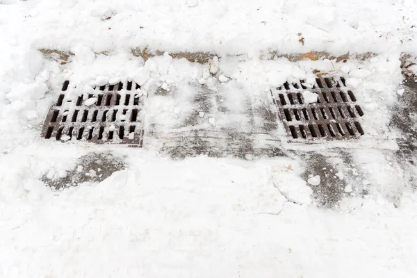 Two storm drains in winter. The drains are shoveled but some snow remains.