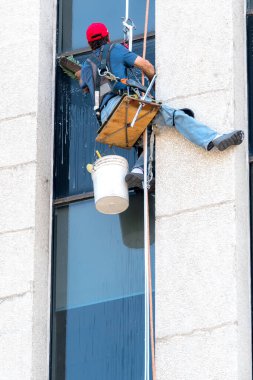 Yüksek bir binada çalışan kimliği belirsiz bir cam silici. Halatla asılmış çok küçük bir platformda oturur ve büyük bir fırçayla pencereleri siler..