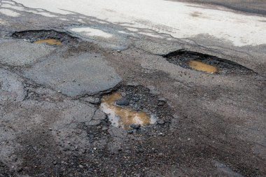 Asfaltlı bir yolda çukurlar. Yol çok kötü bir durumda. Çukurlarda kirli su var..