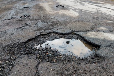 Asfaltlı bir yolda çukurlar. Yol çok kötü bir durumda. Çukurlarda kirli su var..