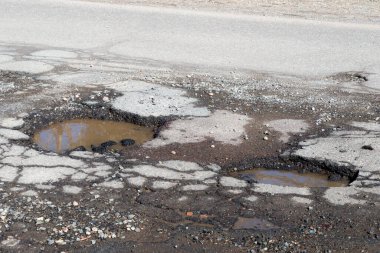 Asfaltlı bir yolda çukurlar. Yol çok kötü bir durumda. Çukurlarda kirli su var..