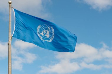 Fundy National Park, NB, Canada - June 30, 2020: United Nations flag flying in the wind on a flagpole against a partially cloudy sky. clipart