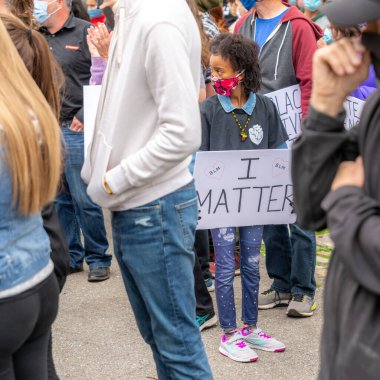 Saint John, NB, Kanada - 14 Haziran 2020: Siyahların Yaşamı Önemlidir rallisi. COVID-19 maskesi takan genç siyah bir kız üzerinde I MATTER yazan bir tabela taşıyor.
