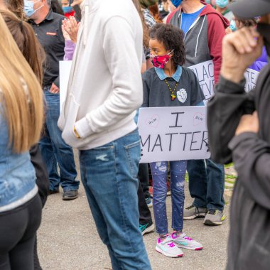 Saint John, NB, Canada - June 14, 2020: Black Lives Matter rally. A young black girl wearing a COVID-19 mask carries a sign that reads I MATTER clipart
