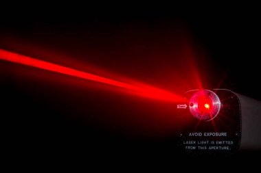 Laboratuvar lazerinden kırmızı lazer ışını. Ön tarafta uyarı uyarısı var. Siyah arka plan. Işın deliğin yakınına yayılır..
