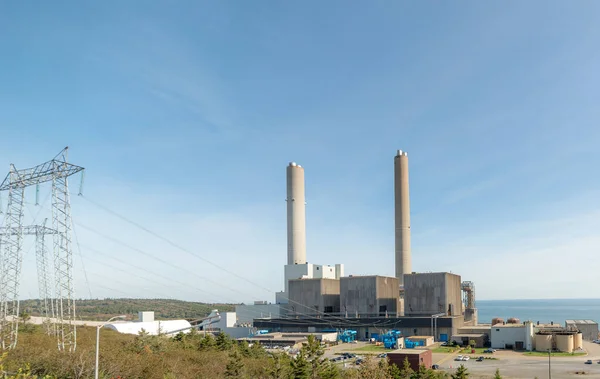 Power generating station. Transmission tower on the right. Large smoke stacks, no smoke. Blue transformers in front of building. Room for text above.