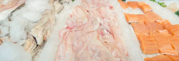 Assorted fillets of fish on ice at a fish market.  Focus is on the center.