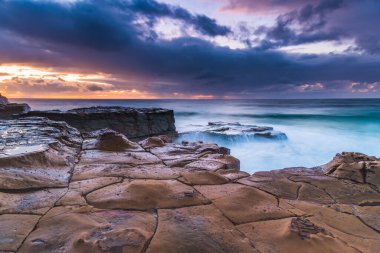 Cloudy sunrise and tessellated rock platform from North Avoca Beach on the Central Coast, NSW, Australia. clipart