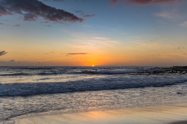 Kumsalda sabahın erken saatlerinde güneş ufuktan yükselirken MacMasters Sahili 'nden, NSW, Avustralya.