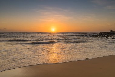 Kumsalda sabahın erken saatlerinde güneş ufuktan yükselirken MacMasters Sahili 'nden, NSW, Avustralya.