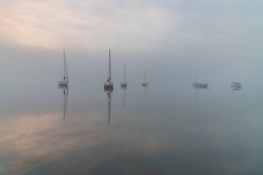 Yoğun bir sis bulutuyla kaplı tekneler, körfezin üzerindeki sisin içinde beliriyor. Koolewong Merkez Sahili, NSW, Avustralya.
