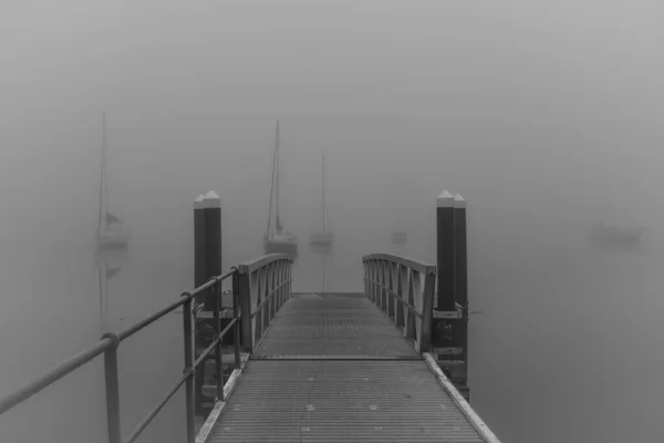 Yoğun bir sis botu iskelenin üzerinde ve körfezin üzerindeki sisin içinde beliriyor. Monochrome 'da Koolewong' da Merkez Sahili, NSW, Avustralya.