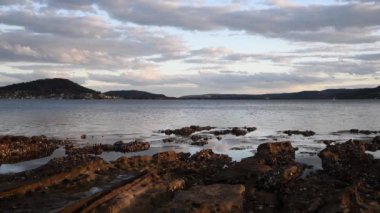 Öğleden sonra geç saatlerde su üzerindeki bulutlar ve kıyıdaki kayalık istiridye örtüsü. NSW, Avustralya 'nın merkez kıyısındaki Point Frederick' ten Brisbane Water.