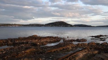 Öğleden sonra geç saatlerde su üzerindeki bulutlar ve kıyıdaki kayalık istiridye örtüsü. NSW, Avustralya 'nın merkez kıyısındaki Point Frederick' ten Brisbane Water.