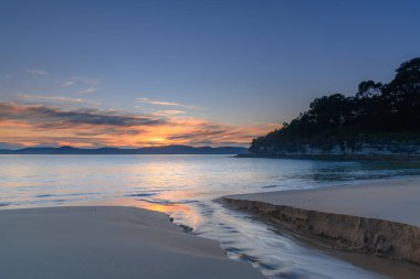 Sakin denizler ve yumuşak bulutlar gündoğumunu gölden süzülen suyla karşıladı. Central Coast, NSW, Avustralya 'daki Pearl Beach' e geri döndü..