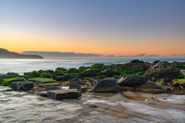 Gündoğumu deniz manzarası yeni taşlarla örtüldü ve kumsaldaki erozyondan sonra Central Coast, NSW, Avustralya 'daki Killcare Sahili' nde yer değiştirdi..