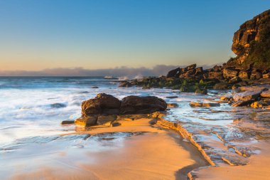 Gündoğumu deniz manzarası yeni taşlarla örtüldü ve kumsaldaki erozyondan sonra Central Coast, NSW, Avustralya 'daki Killcare Sahili' nde yer değiştirdi..