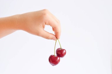 İki sulu kiraz meyvesi çocuğun elinde beyaz arka planda taze kiraz beyaz zemin üzerinde