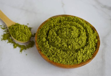 Moringa tozu ahşap kaşıkta ve taze yapraklarla