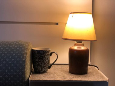 Masa lambası, kahve fincanı ve yatak odası masanın üstünde.