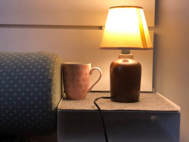 Masa lambası, kahve fincanı ve yatak odası masanın üstünde.
