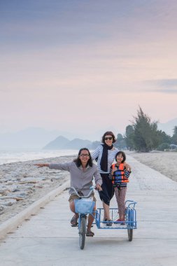 Asyalı aileler güzel bir günde plajda üç tekerlekli bisikletin keyfini çıkarırlar..