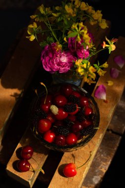 Çiçekler, kirazlar ve kirazların yanı sıra dutlardan oluşan natürmort yaşam bileşimi