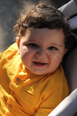 Sarı tişörtlü, gülümseyen fotoğraf portresiyle beyaz görünümlü kıvırcık çocuk.